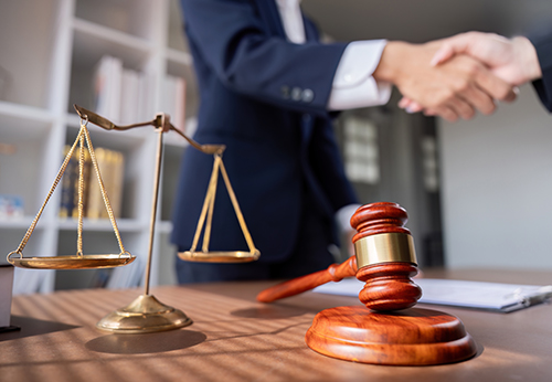 Legal gavel and scales of justice with two people shaking hands.